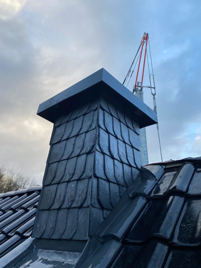 Das Bild zeigt ein neu gedecktes Dach und einen mit Schiefer verkleideten Schornstein, eine professionelle Umsetzung im Bereich Fassadenbau bei Firstetage Leverkusen.