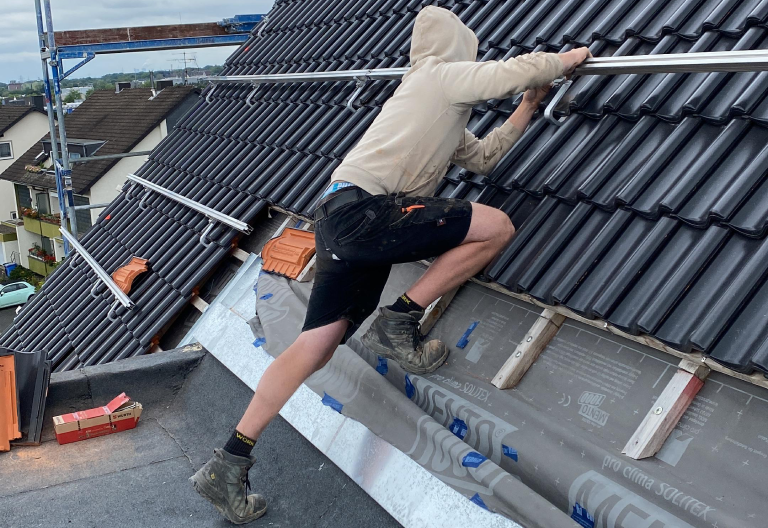 Zu sehen ist ein Mitarbeiter von Firstetage Leverkusen bei der Installation von Halterungen für eine neue Photovoltaik Anlage.