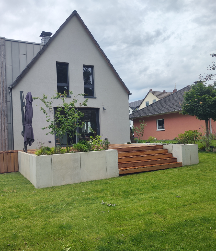 Man sieht ein Einfamilienhaus mit einem neuen Terrasse und Treppe von der Terrasse in den Garten. Im Rahmen von Terrassenbau der Firma Firstetage Leverkusen umgesetzt.